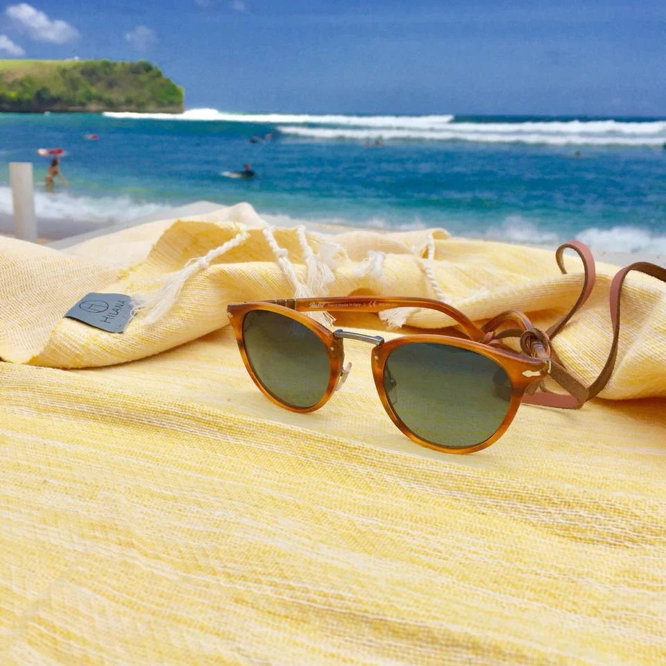 Sunglasses on top of a yellow Hilana Upcycled Cotton Turkish Towel at the beach.