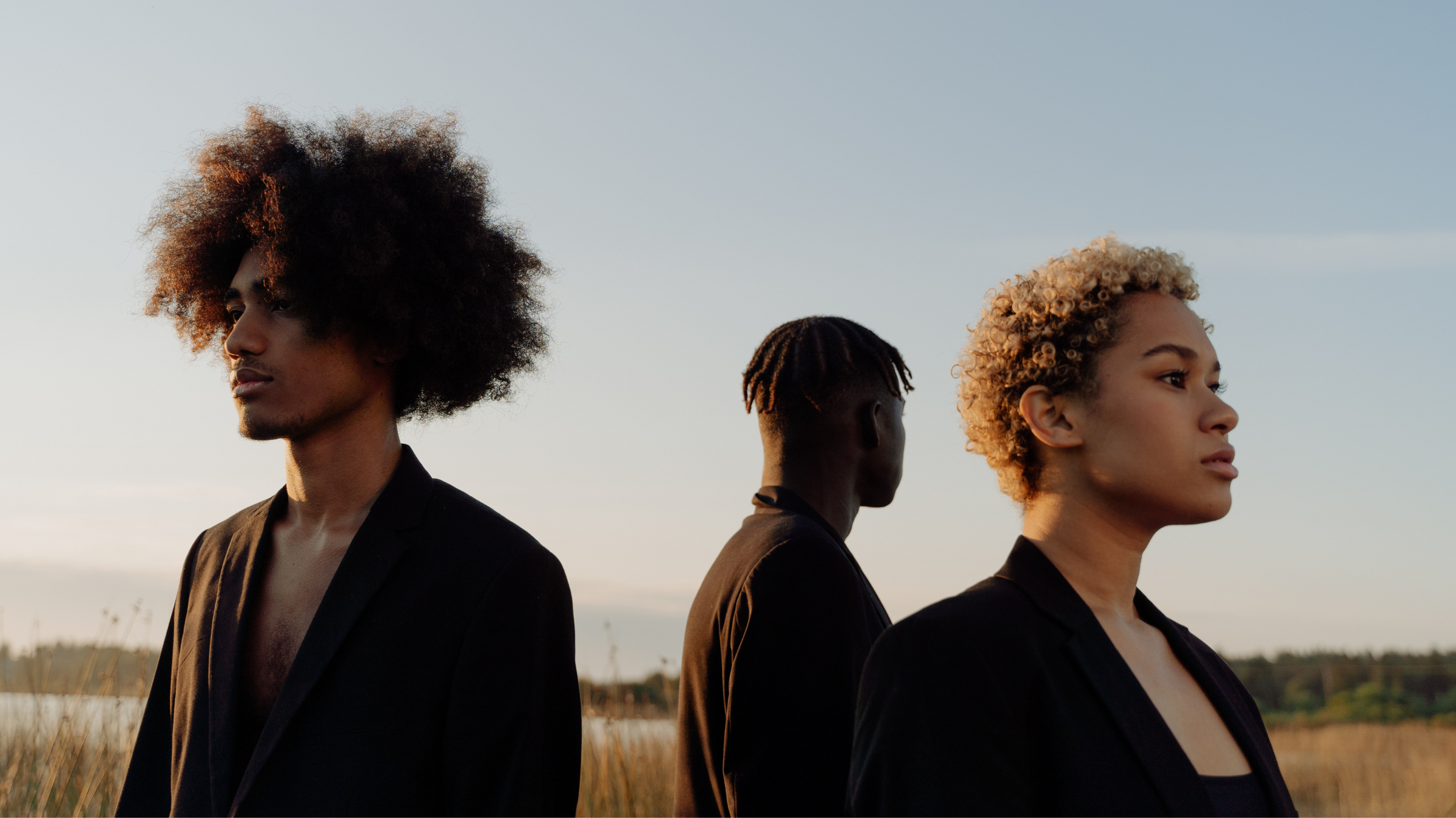 two black men and a black woman in blazers are standing in field